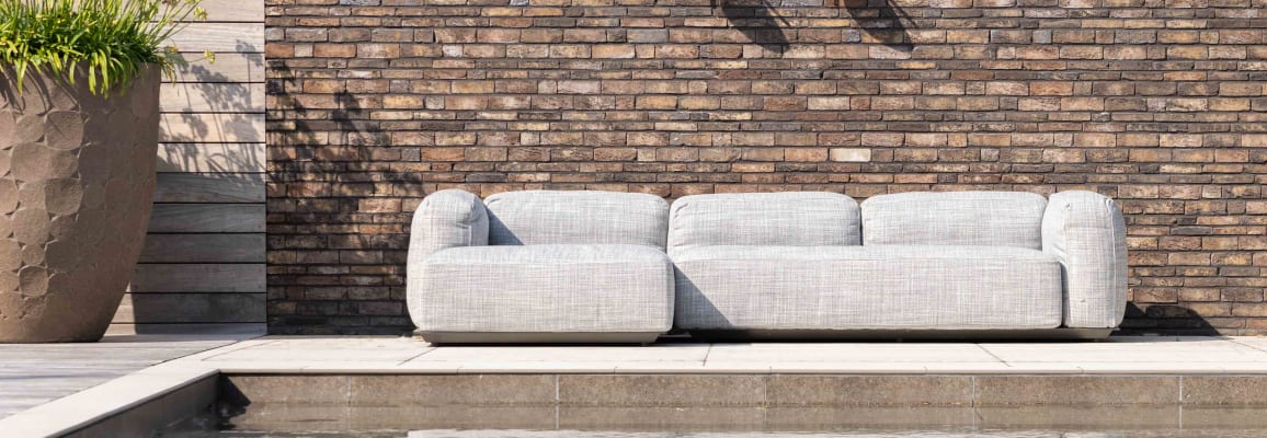 A modern brick wall uses a variety of grey and brown tones. In front of the wall is a low couch.