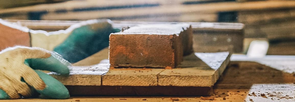 A brick on a table next to a pair of gloved hands.