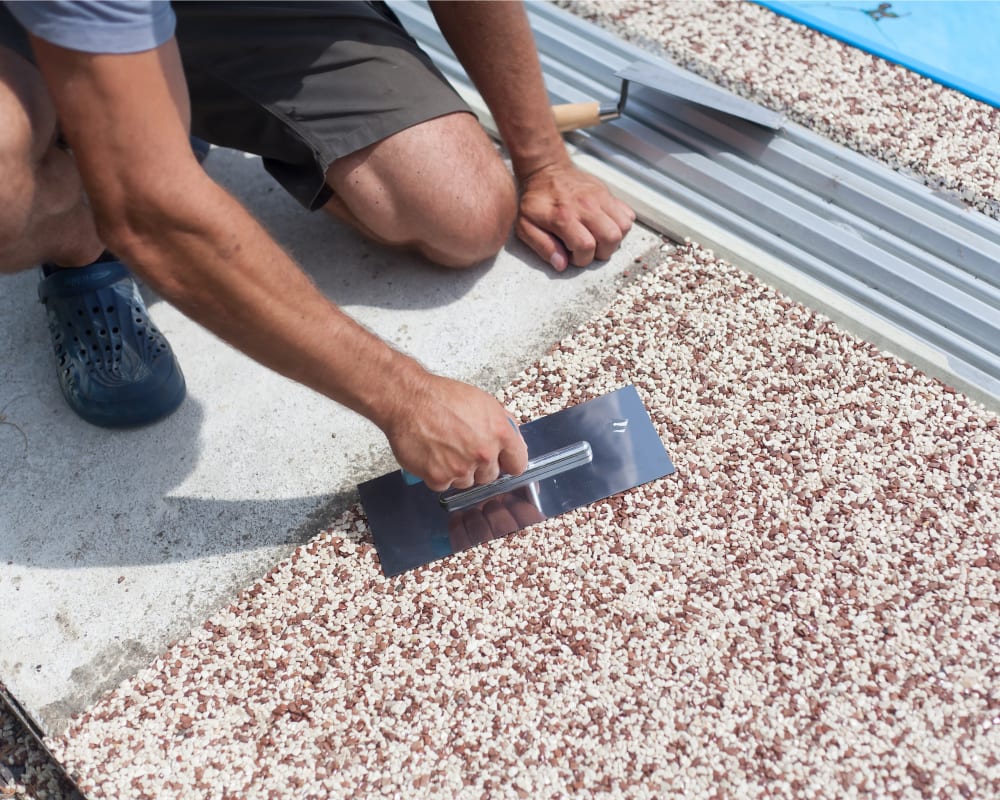 A man finishes a stylized concrete path around a pool.