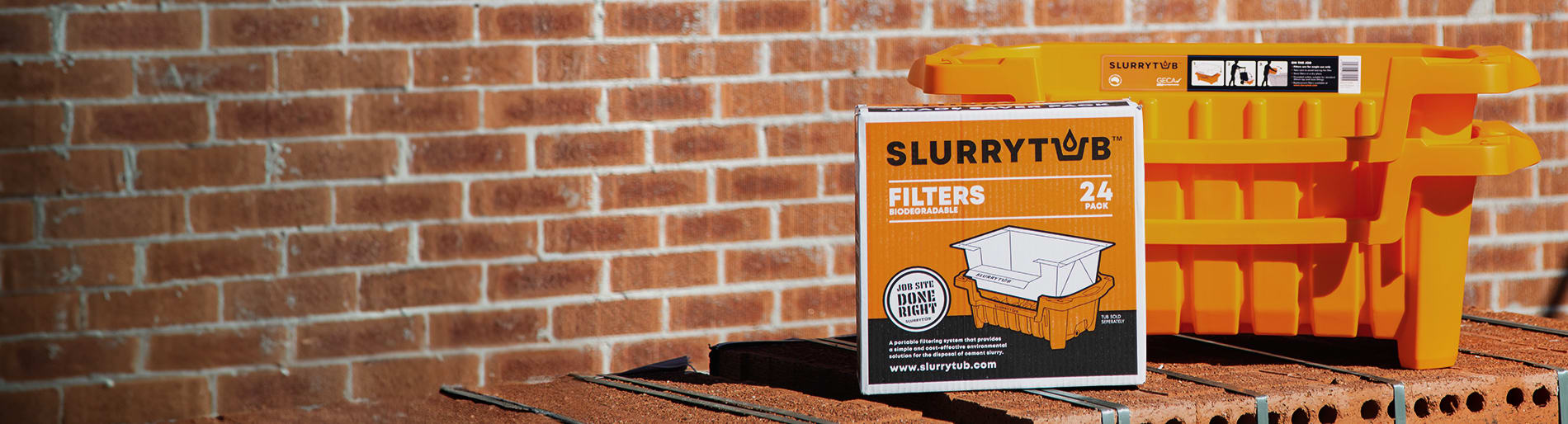 Two orange Slurrytub buckets with a box of filters sitting on top of a stack of bricks in front of a red brick wall.